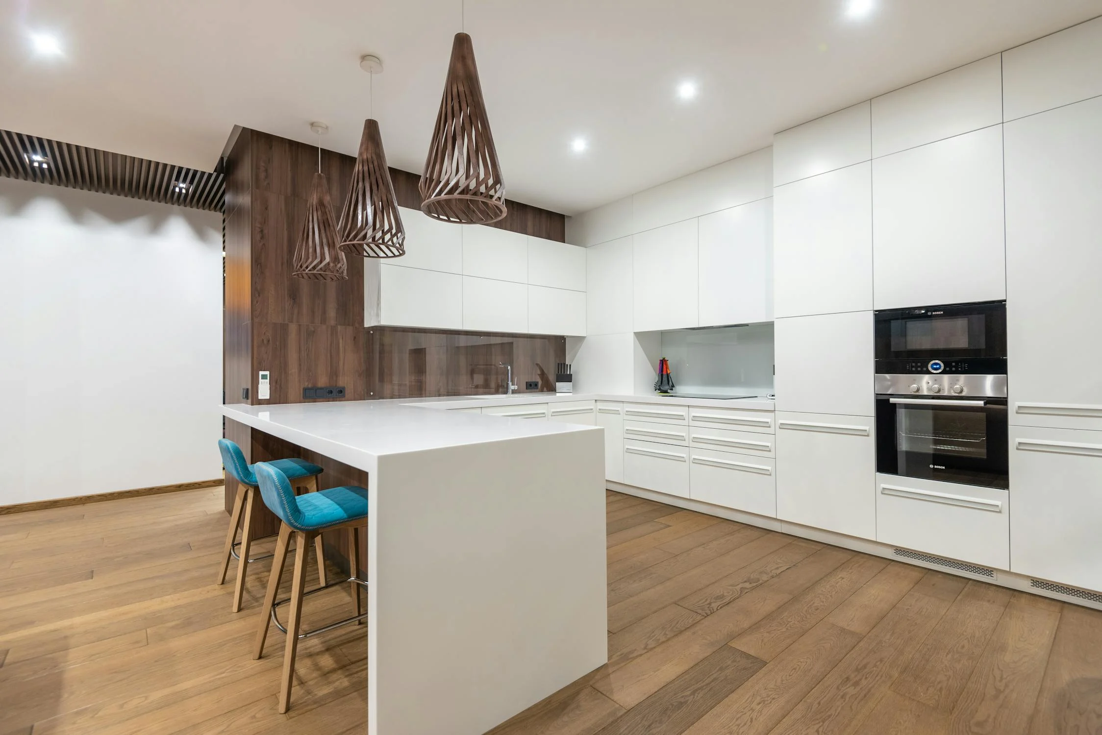 Modern kitchen with white cabinets, wooden accents, a large island, built-in appliances, and blue bar stools under pendant lights.